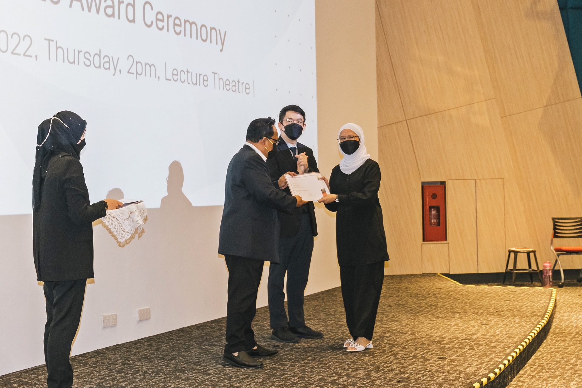A student receives her certificate of completion from Zamahari bin Haji Saidi as Ir Professor Sim Kwan Yong looks on. 