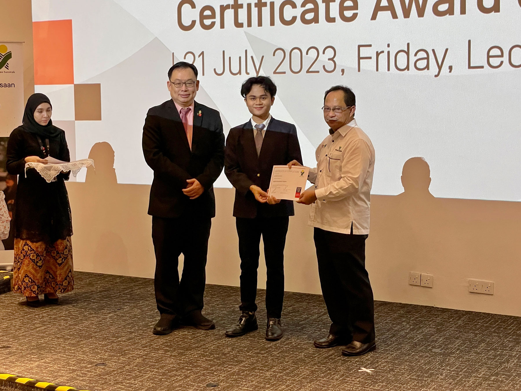 Jilli receives his certificate of completion from Mr Louis (right) as Professor Lau looks on.