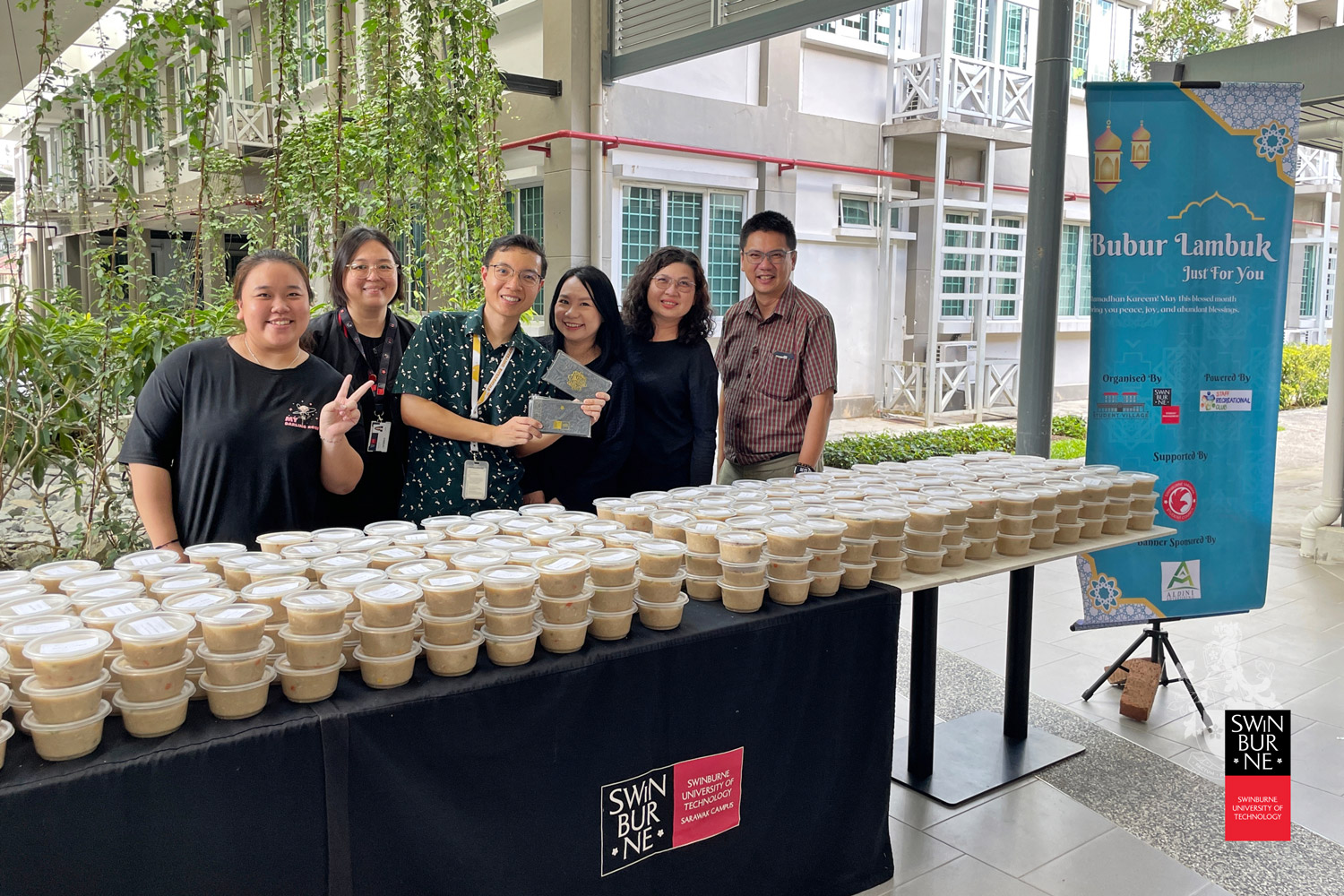 Swinburne Sarawak staff and students take a group photo featuring the packed bubur lambuk ready for distribution. 